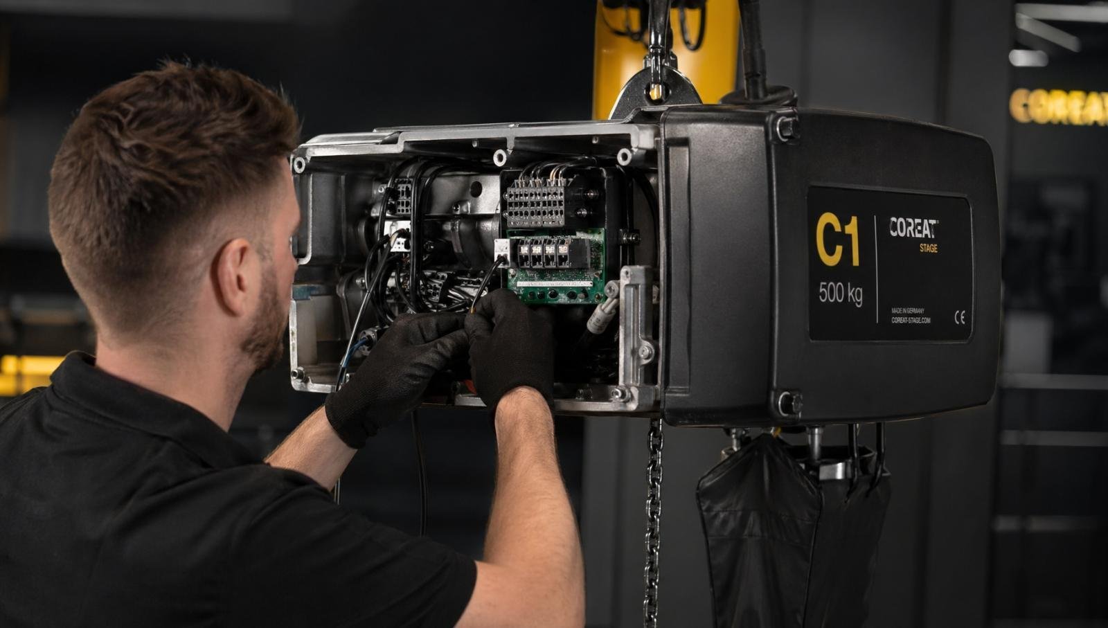 An assembly technician carefully wiring the internal parts of a stage hoist